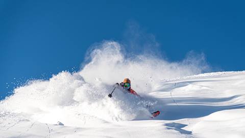 Male skier makes a powder turn under a blue sky at Solitude Mountain Resort